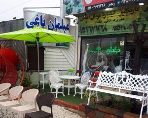 محوطه بیرونی فروشگاه مبلمان باغی همراه با نیمکت آلومینیومی سفید ست چهارنفره طاووسی و صندلی های پلیمری و چتر و تاب