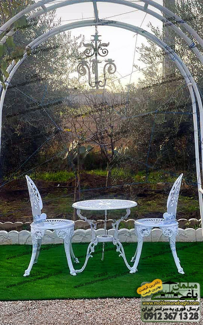میز و صندلی آلومینیومی دو نفره مدل طاووسی به رنگ سفید بر روی چمن مصنوعی در محوطه فضای باز باغی زیبا